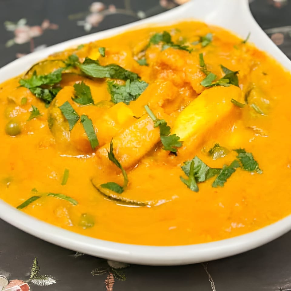 Close-up of a vibrant orange Indian curry with paneer and green peas, garnished with fresh cilantro.