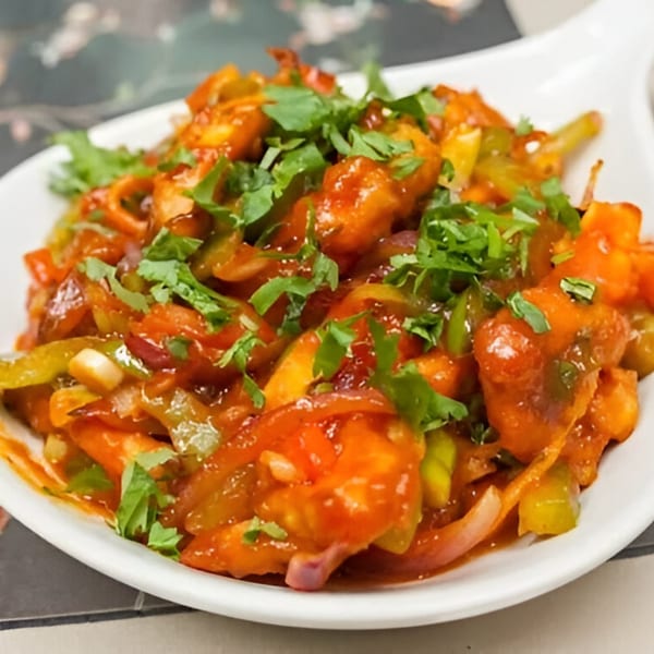 A vibrant Indian dish with chicken, bell peppers, and onions in a rich red sauce, garnished with cilantro.