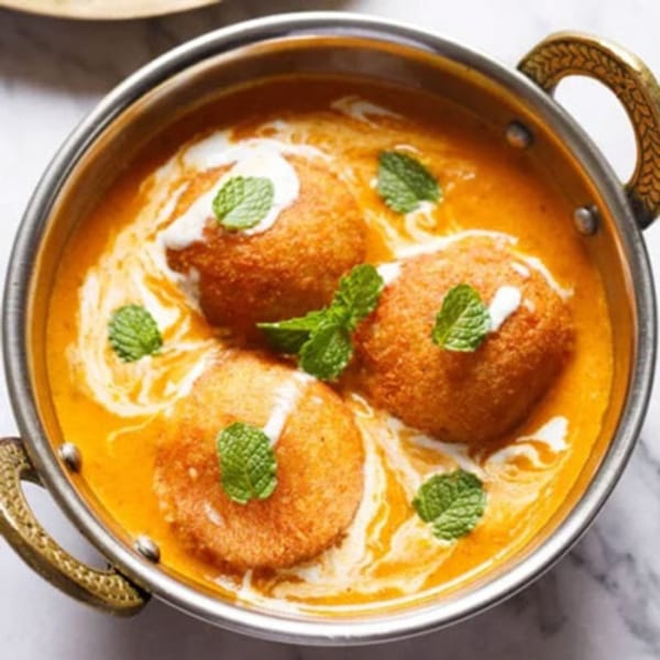 Three golden-brown Indian kofta balls in a rich orange curry sauce, garnished with fresh mint leaves.