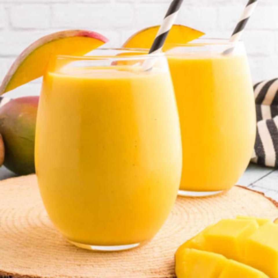 Two glasses of mango lassi with striped straws, garnished with mango slices.