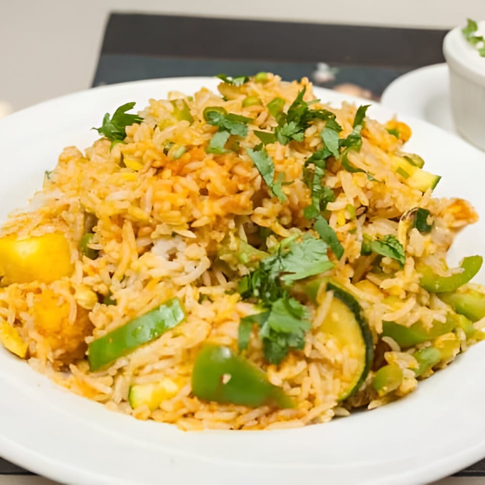 Close-up of Indian vegetable biryani with rice, green peppers, zucchini, and cilantro on a white plate.