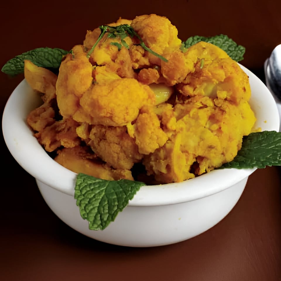 A white bowl filled with golden-fried Indian cauliflower and potato pakora, garnished with fresh mint leaves.